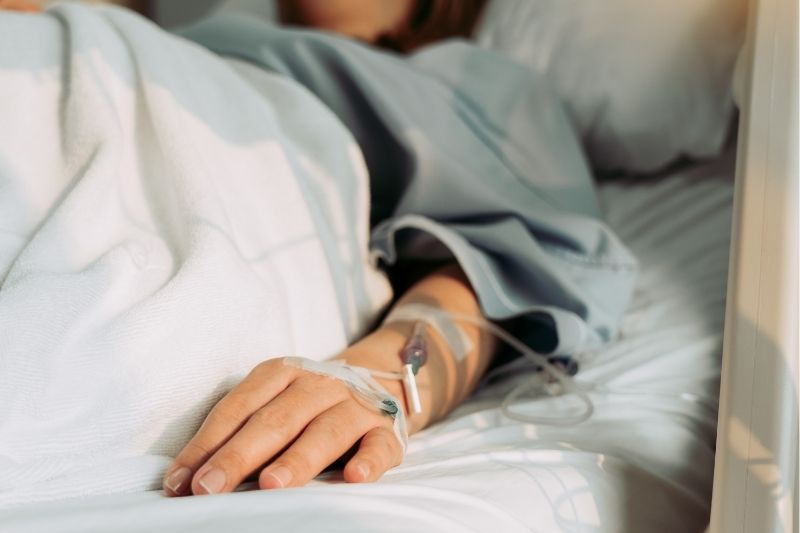 Woman lying on hospital bed with drip attached to hand